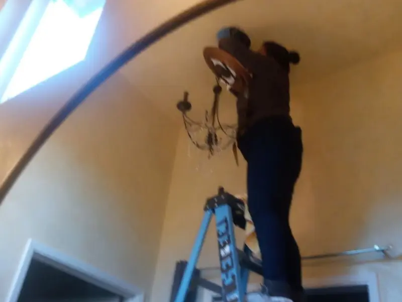 Electrician installing a chandelier in a Henrietta residence